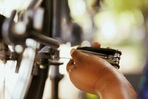 Bild präsentieren weiblich Hand mit spezialisiert Ausrüstung zu einstellen das Ventil auf Fahrrad Rad. detailliert Schuss von afrikanisch amerikanisch Person Ausbessern Fahrrad vorsichtig mit Mehrzweck Werkzeug. foto