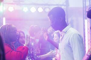 afrikanisch amerikanisch Paar zeigen Hände bewegt sich während improvisieren tanzen Schlacht im dunkel Nachtclub beleuchtet mit Beleuchtung. jung Tänzer Party machen beim Diskothek im überfüllt Verein foto