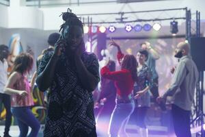 afrikanisch amerikanisch Mann Abdeckung Ohr während versuchen zu Plaudern auf Handy, Mobiltelefon Telefon im Nachtclub. jung Clubber Stehen auf Tanzfläche und reden auf Smartphone während Musik- spielen laut im Verein foto