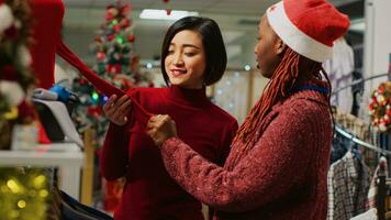 asiatisch Kunde interessiert im rot Bluse zu tragen während Winter festlich thematisch Party, fragen Mitarbeiter Über Materialien und Preis. Klient im brauchen von Weihnachten Kleidung zum Weihnachten Feierlichkeiten foto