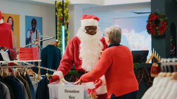 Verkauf Assistent gekleidet wie Santa claus Sammeln unnötig Kleider von Kunden im Spende Kasten, geben Sie wie Geschenk zu jene im brauchen während Weihnachten Jahreszeit, Verbreitung Urlaub jubeln foto