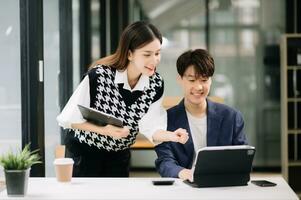 asiatisch Geschäft Kollege Geschäft die Geschenke und erklärt und mit Laptop und Tablette. Zusammenarbeit, finanziell Marketing Team, während Sitzung im modern Büro Zimmer. foto