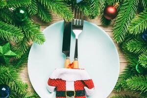 Draufsicht auf Gabel, Messer und Teller, umgeben von Tannenbaum und Weihnachtsdekorationen auf Holzhintergrund. konzept für silvester- und feiertagsdinner foto