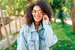 schließen oben emotional Porträt von froh ziemlich gemischt Rennen Dame spielen mit ihr tolle lockig afro Haare. draussen. foto