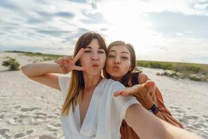 zwei Frauen lächelnd und posieren zum das Kamera auf das Strand foto