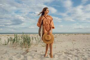 ein Frau im ein Orange Kleid und Hut auf das Strand foto