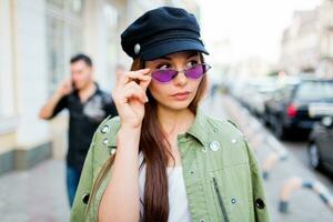 spielerisch Frau posieren draussen . tragen modisch lila retro Brille , schwarz Deckel . schließen oben Porträt . windig Haare. Lebensstil Bild. foto