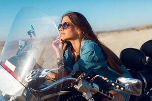 jung tolle sexy Frau Sitzung auf Motorrad auf das Strand, tragen stilvoll Ernte oben , Hemden, haben perfekt passen schlank gezähmt Körper und lange Haare. draussen Lebensstil Porträt. foto