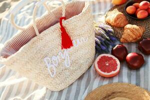 Sommer- Picknick auf das Strand - - Croissants, Äpfel, Erdbeeren und Süßigkeiten. modisch Stroh Tasche. foto