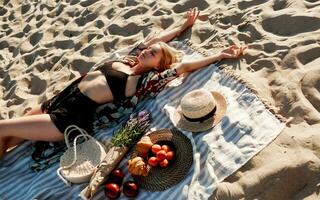 verführerisch blond Frau Lügen auf das Sand während Ausgaben Zeit auf Picknick auf das Strand. foto