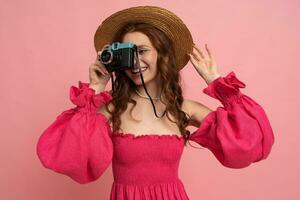 glücklich Reisender Frau im Stroh Hut und Rosa Kleid halten retro Kamera. Studio Foto. Rosa Hintergrund. foto