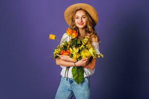 Studio Mode Porträt von ziemlich süß blond Frau im Stroh Hut, Weiß Baumwolle Hemd Sitzung und halten Strauß von tolle Frühling Blumen. tragen stilvoll retro Outfit . foto