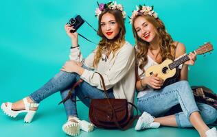 Studio Lebensstil Porträt von zwei ziemlich jung blond glücklich Mädchen haben Spaß. Herstellung Bilder im Hipster Stil auf retro Kamera, tragen stilvoll Jahrgang Boho Outfits und Blumen Kranz. Frühling. foto