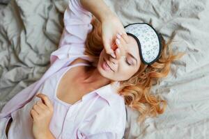 ziemlich Frau mit offen Lächeln posieren im Auge Maske beim Zuhause und Trinken heiß Tee. gemütlich Zuhause Atmosphäre. foto