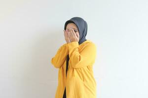 jung schön asiatisch Muslim Frau, tragen Brille und Gelb Blazer mit Hand Geste Abdeckung Gesicht foto