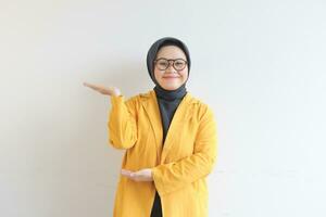 schön jung asiatisch Muslim Frau, tragen Brille und Gelb Blazer zeigen Palmen während lächelnd foto