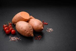 frisch groß Rosa Süss Kartoffel Knollen mit Tomaten und Gewürze auf ein dunkel Hintergrund foto