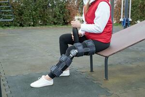 Frau, die nach einer Beinoperation eine Knieorthese oder Orthese trägt und im Park spazieren geht foto