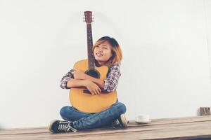 schöne Frau sitzt mit ihrer Gitarre glücklich auf dem Holz sitzend foto