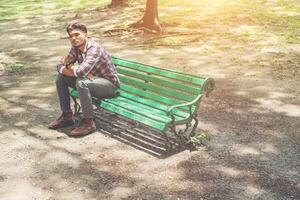 junger Hipster-Mann sitzt auf einer Holzbank im Park. foto