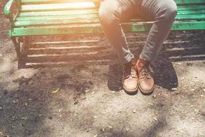 Hipster-Typ sitzt auf einer Bank mit Jeans und braunen Gämsenschuhen. foto
