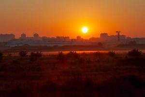 Morgendämmerung über der Stadt mit kontrastierendem orangefarbenem Himmel und Nebel auf dem Feld foto