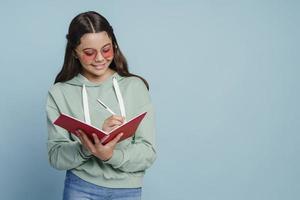 lächelndes, süßes Teenager-Mädchen mit Sonnenbrille, das ein Notizbuch hält foto