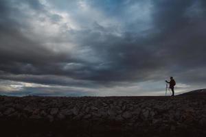 Silhouette eines Fotografen oder Reisenden mit Stativ auf Stein stehend foto