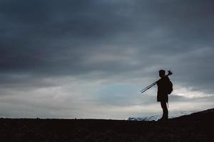 Silhouette eines Fotografen oder Reisenden mit Stativ auf Stein stehend foto