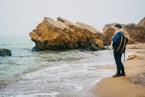 Mann mit Rucksack, der in der Nähe eines Felsens gegen ein schönes Meer steht foto