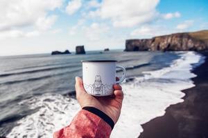 Touristische Tasse in der Hand mit den Bergen auf dem Hintergrund des Meeres foto