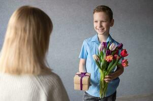 Mama akzeptiert ein Geschenk von ihr Sohn im ein Blau Hemd mit Tulpen im seine Hände foto