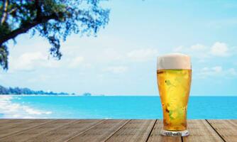 Bier vom Fass oder Craft Beer in einem hohen klaren Glas mit Bierschaum oben und es gibt Blasen im Glas. kaltes bier in einem glas, aufgestellt auf einem holztisch am strand, tagsüber das meer. 3D-Rendering foto