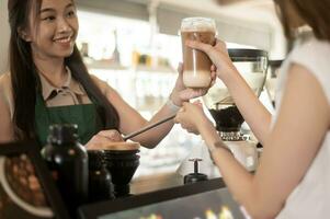 jung asiatisch Bedienung aufgeschlossen Barista mit Kunde im Kaffee Geschäft foto