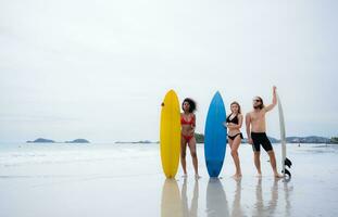 Gruppe von freunde im Badeanzüge posieren mit Surfbretter auf das Strand. foto