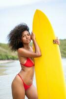 Porträt von lächelnd jung Frau im Bikini mit Surfbrett beim Strand foto
