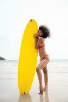 voll Länge Porträt von ein jung Frau mit Surfbrett beim das Strand foto