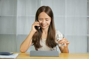 asiatisch Frau Arbeiten beim Zuhause halten ein Glas von Wasser im Hand foto