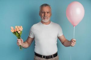 galanter, älterer Mann hält Blumen und rosa Ballon in der Hand foto