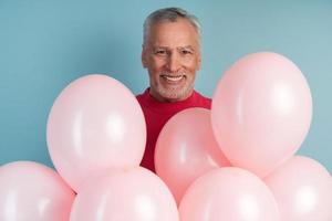 positiver, fröhlicher Mann mit Luftballons, die auf blauem Wandhintergrund posieren foto