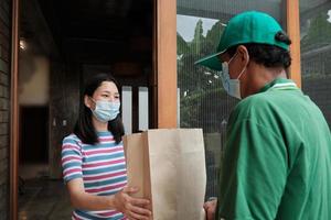 Liefermann mit Gesichtsmaske gibt einer asiatischen Frau ein Paket. foto