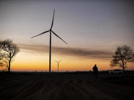 Silhouette eines Mannes geht zum Sonnenuntergang in Richtung Windkraftanlagen foto