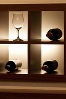 ein leeres Weinglas und drei Flaschen im Regal foto