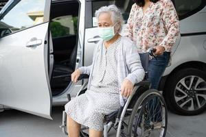 Helfen Sie einer asiatischen Seniorin im Rollstuhl, sich darauf vorzubereiten, zu ihrem Auto zu gelangen foto