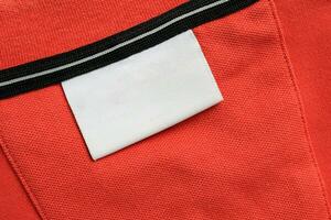 leer Weiß Wäsche Pflege Kleider Etikette auf Orange Hemd Stoff Textur Hintergrund foto