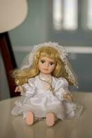 Jahrgang blond Puppe mit Blau Augen im ein Hochzeit Kleid sitzt. foto