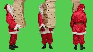 Heilige Nick halten Pizza Kisten, liefern enorm Stapel von schnell Essen Über voll Körper grüner Bildschirm. Santa claus Verkörperung tragen traditionell Dezember Kostüm mit Weiß Bart, Karton Pakete. foto