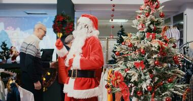 froh afrikanisch amerikanisch Arbeiter gekleidet wie Santa claus im Weihnachten aufwendig Einkaufen Einkaufszentrum Kleidung Geschäft. Mitarbeiter klingeln Weihnachten Glocken und Gruß glücklich Kunden im festlich schmücken Mode Geschäft foto