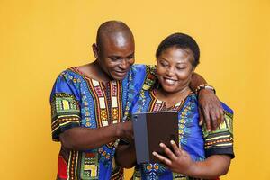 lächelnd Ehefrau und Mann mit froh Ausdruck umarmen während mit Digital Tablette zusammen. heiter Frau halten tragbar Gadget während Mann tippen auf Berührungssensitiver Bildschirm im Studio foto