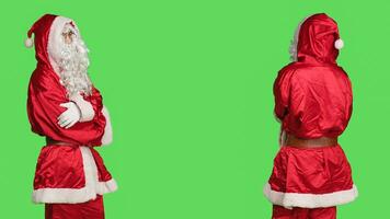 zuversichtlich jung Mann im traditionell Santa claus Kostüm, Komplett mit Weiß Bart und Brille. Stehen Über grüner Bildschirm Hintergrund repräsentiert festlich Geist während Weihnachten Jahreszeit. foto